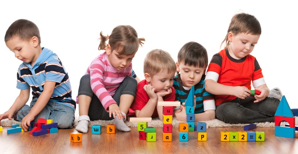 Five kids are playing on the floor with blocks in kindergarten